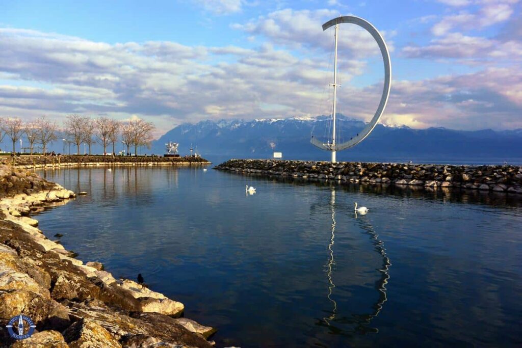 “Lausanne waterfront on Lake Geneva with boats moored at the pier and Alpine hills in the background.”