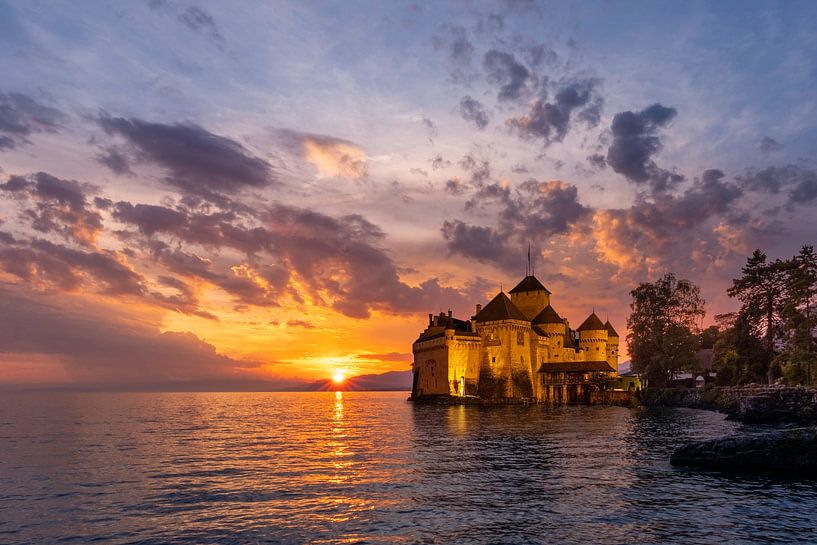 Medieval Château de Chillon on the shores of Lake Geneva at sunset, mountains faintly visible in background.”