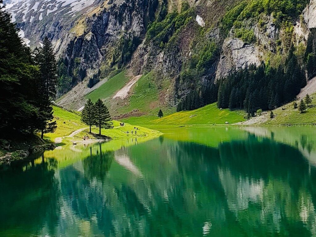 The Äscher mountain guesthouse perched on a sheer rock face with hikers approaching, Alpstein region.
